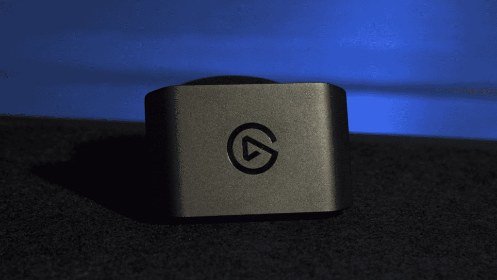 Fotografía de cerca de la capturadora Elgato 4K X junto a una laptop, mostrando lo pequeña y compacta que es en un escritorio ordenado